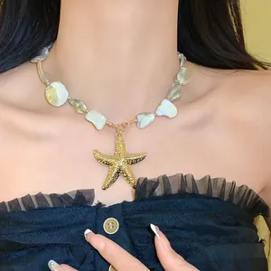 Detailaufnahme einer unregelmäßigen Muschelhalskette mit einem goldenen Seesternanhänger.