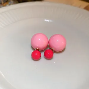 Detailed macro view of pink and red double-sided ball stud earrings on a white plate