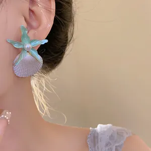 Macro view of stylish ocean-themed earrings featuring a green starfish and shell drop