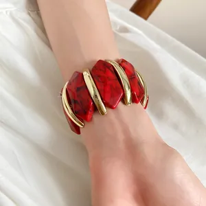 Detailansicht eines elastischen Armbands aus marmoriertem Acryl und Goldmetall am Handgelenk.