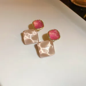 Close-up of elegant pink geometric stud earrings with woven and water ripple textures.