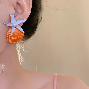 Detailed view of large starfish and orange shell earrings with a pearl center shown on ear