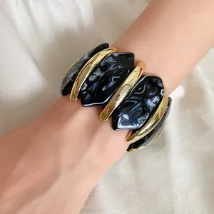 Nahaufnahme eines schwarz marmorierten Acrylarmbands mit goldenen Elementen am Handgelenk