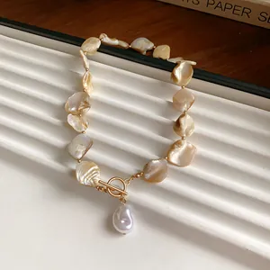 Nahaufnahme unregelmäßiger cremefarbener Muschelfragmente und Barockperle mit Goldverschluss.