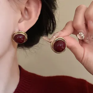 Primer plano de los pendientes vintage de perlas burdeos con diseño de hilo dorado