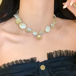 Nahaufnahme einer unregelmäßigen Muschelkette mit goldenem Anhänger im Strandstil.