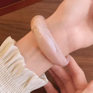 Close-up of elegant pink marbled acrylic open bangle worn on a female wrist with warm lighting
