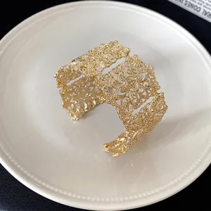 Elegante brazalete ancho dorado con patrón calado para mujer en un plato blanco