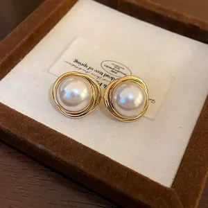 Primer plano de pendientes vintage dorados con grandes perlas de imitación centrales.