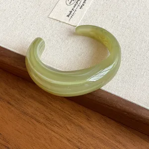 Close-up of a glossy green marbled acrylic open cuff bracelet on a wooden surface.