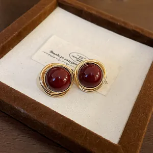 Vista detallada de pendientes vintage dorados con perlas rojo oscuro en un estuche