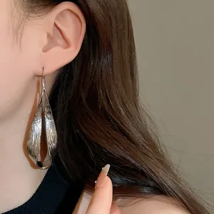 Macro detail of silver irregular twisted metal long drop earrings worn by a model.