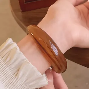 Close-up of glossy amber acrylic bangle with marbled pattern on a slender woman's wrist.