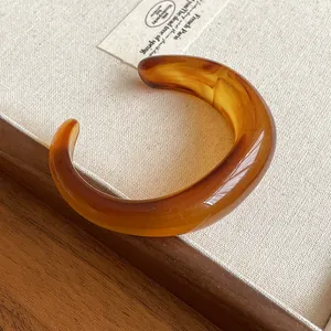 Close-up of a premium glossy amber acrylic open cuff bracelet with elegant marbled texture