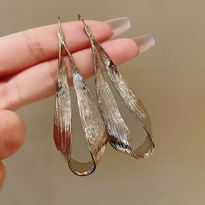 Detailed view of oversized metallic irregular twisted drop earrings with gold finish