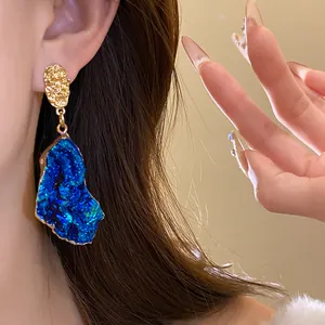 Close-up view of vintage blue irregular drop earrings with textured gold studs.