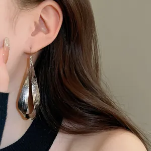 Detailed view of irregular twisted metal teardrop earring on model's ear