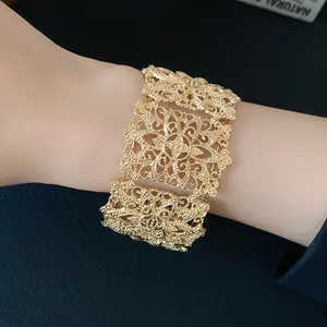 Primer plano de un brazalete ancho dorado con intrincados motivos florales en la muñeca.