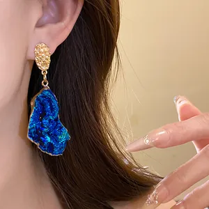Detailed close-up of a vintage style irregular blue druzy stone pendant earring worn on ear