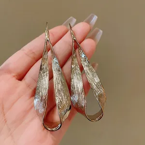 Detail showing the irregular twisted texture of the gold metal dangle earrings.