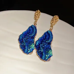 Detailed shot of irregular blue druzy drop earrings with textured gold studs.