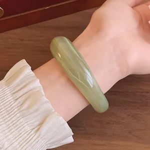 Close-up of a light green marbled acrylic bangle on a wrist with a ruffled sleeve.