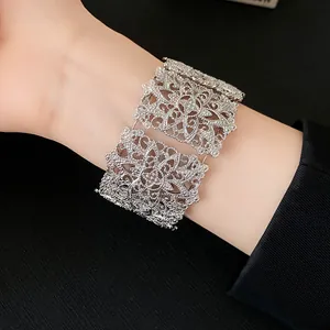Primer plano de un brazalete ancho plateado con diseño de filigrana y flores caladas