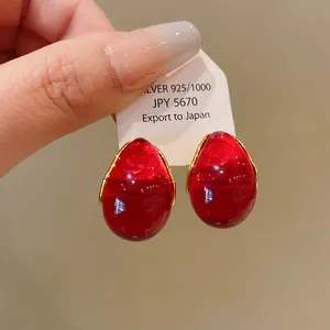 Close-up of teardrop-shaped red resin earrings with gold wire detail on a white tag.