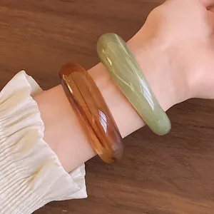 Close-up of elegant marbled acrylic bangles in amber and green worn on a person's wrist