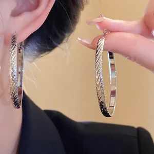 Macro view of silver large hoop earrings with elegant diagonal pleated texture.