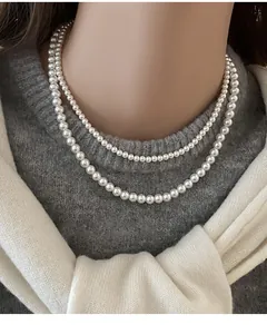 Gros plan d'un élégant collier de perles à double rang sur un mannequin en pull gris