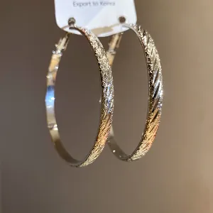 Macro detail of silver-toned hoop earrings showing a glittery texture and diagonal ridges