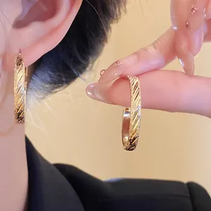 Close-up detail of gold hoop earrings with elegant diagonal textured engraving