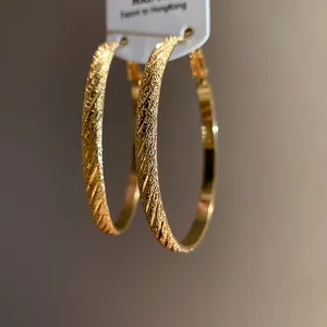 Macro view of gold hoop earrings with sandblasted texture and diagonal striped design