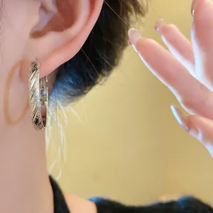 Close-up detail of silver hoop earrings featuring diagonal stripes and a textured finish