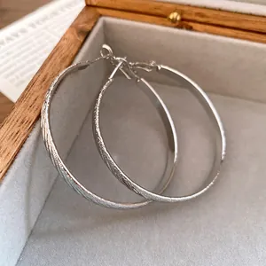 Detailed macro view of silver hoop earrings featuring unique pleated diagonal textures.