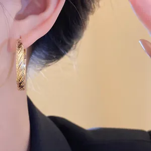 Close-up of gold hoop earrings with diagonal pleated texture on model