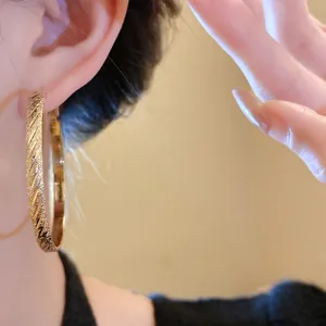 Close-up of gold-plated hoop earring featuring a textured diagonal striped pattern.
