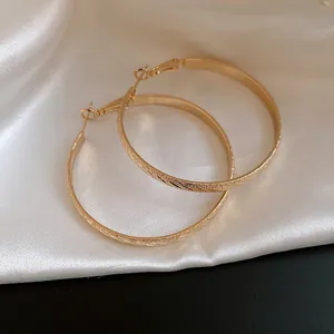 Close-up detail of large gold hoop earrings with elegant textured diagonal pattern