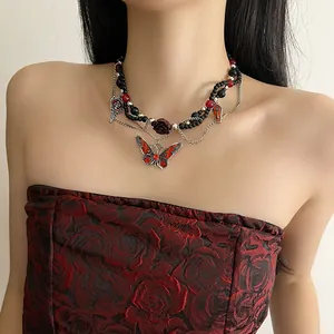 Detalle de collar gótico con cuentas negras, mariposa roja y colgante de rosa de resina.