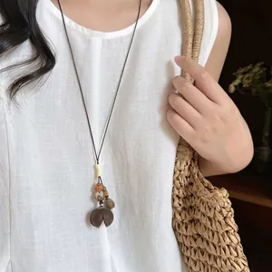 Ethnic style wax cord necklace with wooden beads and pinecone pendant on white linen