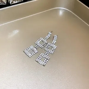 Dettaglio di eleganti orecchini quadrati a pendente con strass su vassoio in metallo