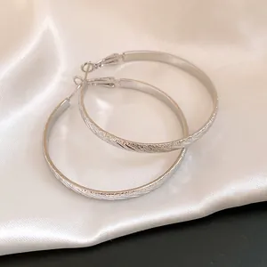 Detail view of silver hoop earrings featuring a unique corrugated twill texture pattern.
