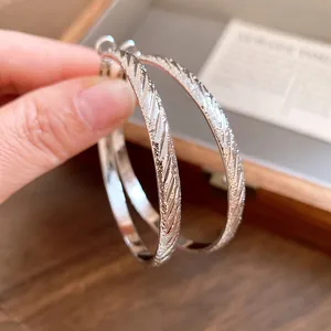 Macro view of silver hoop earrings featuring textured diagonal patterns and frosted finish