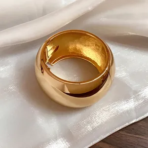 Bold minimalist chunky gold metal bangle with high-gloss finish and elastic hinge closure