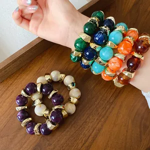 Primo piano di braccialetti in perline acriliche colorate con tocchi dorati su legno.