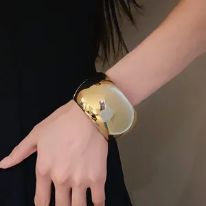 Close-up of a wide polished gold cuff bracelet on a female wrist with metallic shine