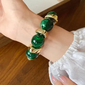 Primo piano di un bracciale a catena in acrilico marmorizzato verde e perle dorate al polso.