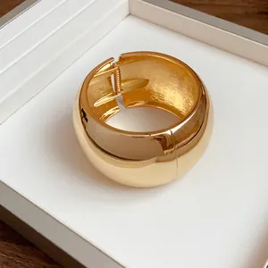 Close-up of a wide polished gold metal cuff bracelet with hinged spring opening