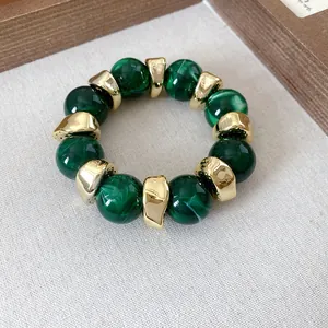 Dettaglio del bracciale con perle in acrilico verde marmorizzato e distanziatori dorati.